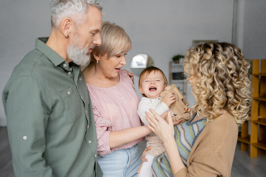 offended child holding toy car and crying near mother and grandparents at home.