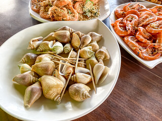 Various delicious seafood dishes in a white plate bowl on a wooden table. Sea Snails, prawns, shrimps, mussels, lobster, crabs, fish. Close-up top view high angle.