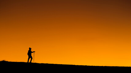 alone hiker hiking is silhouette walking on  mountains, sunset. Ascending a mountain peak at sunset with the silhouette in the background. sport and adventure. Weekend activities. walks on mountains