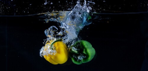 Fototapeta na wymiar Yellow and green bell peppers in water, black background