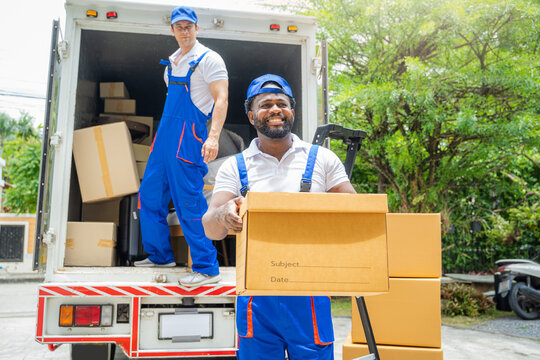Two removal company workers are unloading boxes from a mini truck into new home.