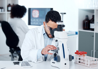 Obraz premium A serious medical scientist sitting at a desk and using a microscope to examine and analyse test samples on slides. Hispanic healthcare professional discovering a cure for diseases in his laboratory