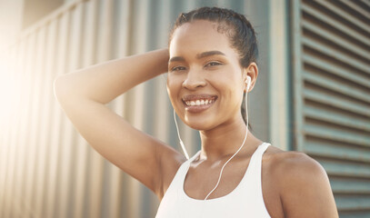 Fototapeta na wymiar Portrait of one confident young hispanic woman listening to music with earphones while exercising in an urban setting outdoors. Determined female athlete looking happy and motivated for training