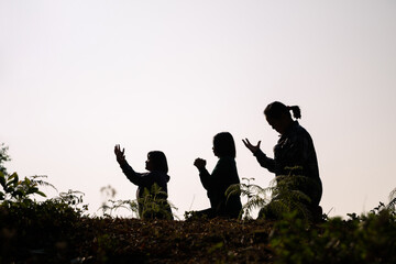 Silhouette of three woman kneeling down praying for worship God at white background. Christians...