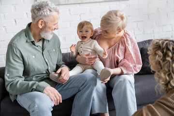 carefree child laughing near happy grandparents and blurred mother in living room.