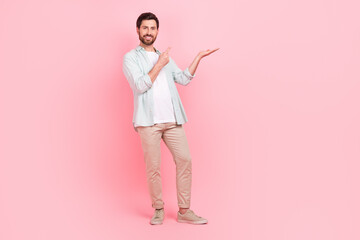 Full size photo of attractive young man palm hold finger point empty space dressed stylish blue outfit isolated on pink color background