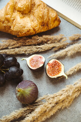 Autumn attributes. Croissant, dark grapes, book and figs on the grey table. Gold October