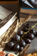 Autumn attributes. Croissant, dark grapes, book and figs on the grey table. Gold October