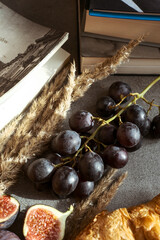 Autumn attributes. Croissant, dark grapes, book and figs on the grey table. Gold October