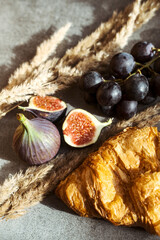 Autumn attributes. Croissant, dark grapes, book and figs on the grey table. Gold October