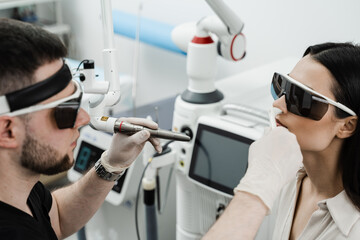 ENT doctor in protective glasses holding surgical laser and doing laser treatment inflammation of the nasal lining, runny nose, sneezing symptoms. Chronic rhinitis treatment with laser.