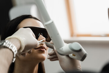 ENT doctor with laser treats girl patient in protective glasses. Laser treatment inflammation of...