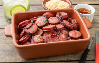 Grilled calabrese sausage portion with onion, farofa and caipirinha over wooden table