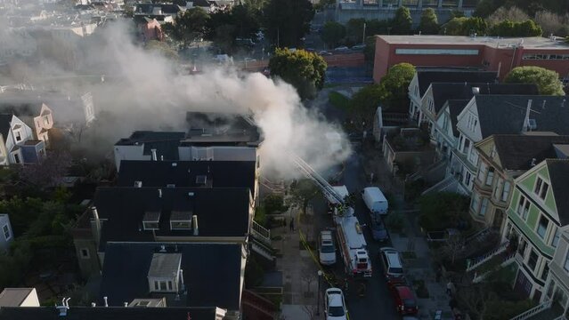 Fly above street in residential urban borough. Firefighters fighting with house on fire. Thick smoke rising from blaze.