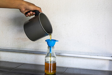 A man is pouring used cooking oil into a glass bottle.