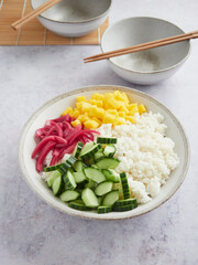 colorful vegetarian poke bowl with rice, mango, cucumber and pickled red onion. Ready to serve, bowl and chopsticks at the the bottom.