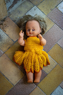 Old doll in orange woolen dress lying on the floor