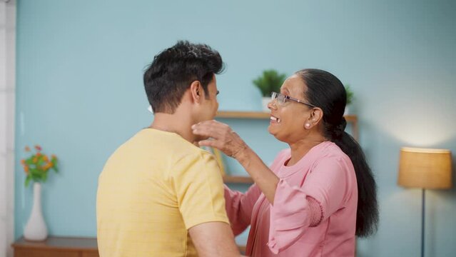 Happy Indian son wishing Mother day by giving greeting card and flowers to elderly mother at home - concept of relationship, bonding and enjoyment - Powered by Adobe