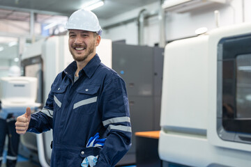 Male engineer showing thumbs up and standing at factory. Smiling technician wearing uniform and...
