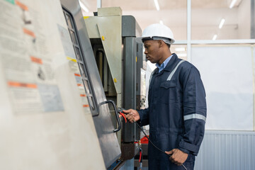 Male engineer using CNC machine in control panel at factory. Man technician in uniform and helmet safety working at workshop heavy metal industrial