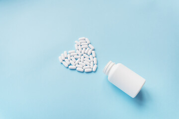 White pills in the shape of a heart came out of a jar on a blue background, health and heart...