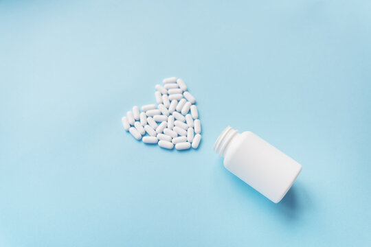 White pills in the shape of a heart came out of a jar on a blue background, health and heart problems together with a plastic jar. The concept of medicine and health care.