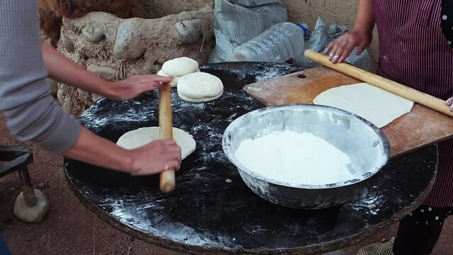 Women's hands roll out wooden rolling pin on table sprinkled with flour yeast dough for dish baursaks. Traditional bread of the Kyrgyz, Tajiks, Uzbeks in form of pieces fried in large amount of oil