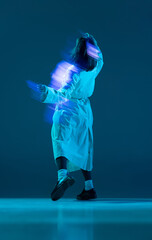 Fototapeta premium Portrait of female body wearing long coat posing with reflection of glow on body over turquoise mode background. Mixed neon light. Back view