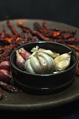Curly dried chilies, shallots and garlic on a clay plate, on a wooden board.
