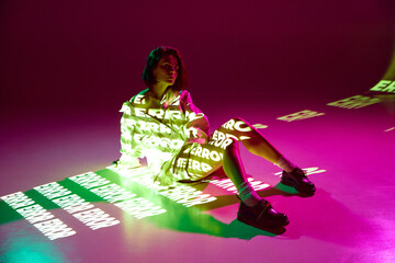 Portrait of dreaming girl sitting on floor with digital neon filter lights with inscryption on body on pink mode background. Error, mistake