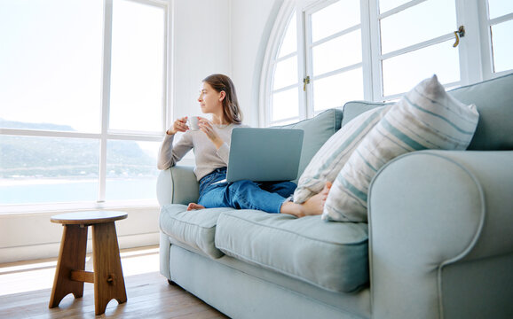 Some Time Alone With My Thoughts. Full Length Shot Of An Attractive Young Woman Looking Thoughtful While Relaxing On The Sofa At Home.