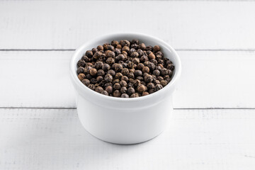 Black pepper seeds bowl. 45 degrees studio shoot on light wooden background.