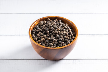 Black pepper seeds bowl. 45 degrees studio shoot on light wooden background.