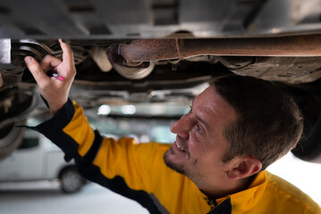 Auto repair mechanic the undercarriage of the car is being inspected for damage caused by heavy collisions.