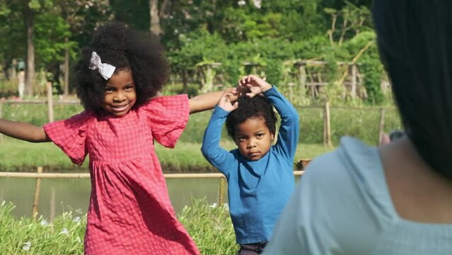Black girl and boy with wavy hair are posing for their mothers to take pictures in the park.