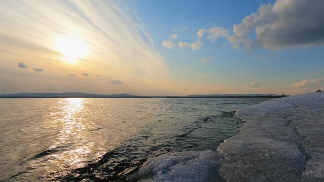 Time lapse overlooking the lake at sunset. On the shore, the last unmelted ice. Beautiful clouds in the sky and the sun.