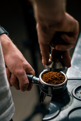 A professional barista in a coffee shop prepares ground coffee by tamping fresh ground coffee beans close-up