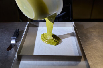 The pastry chef pours the dough into a baking dish in the restaurant kitchen. Green pistachio dough