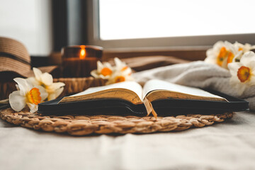 Open Bible with flowers and candles in a cozy home interior. Christian beautiful morning photography.