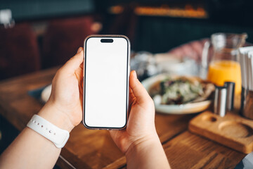 Girl holding a phone with a blank screen in a cafe, with food in the background