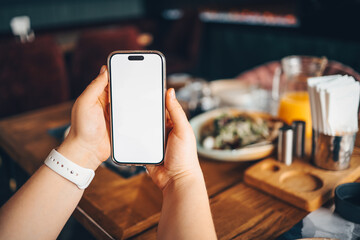 Girl holding a phone with a blank screen in a cafe, with food in the background