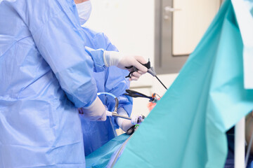 Operacja laparoskopowa na sali operacyjnej w szpitalu. Dłonie chirurga w sterylnych rękawiczkach trzymają narzędzia endoskopowe. Asysta instrumentariuszki. - obrazy, fototapety, plakaty