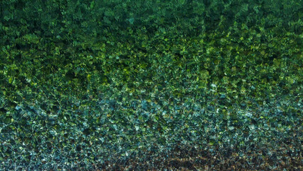 Top view of transparent water sea with stone and pebbles bottom. Sun glare on the surface crystal...
