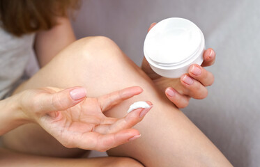 Young woman applying moisturizing body cream on the legs. Body care at home. Close-up. Selective focus.