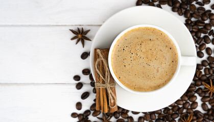 Cup of fresh coffee, cinnamon sticks and scattered coffee beans on a white wooden background. Coffee day. Close-up. Top view. Place for text. Selective focus.