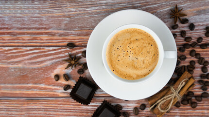 Cup of fresh fragrant cappuccino, chocolate candies and cinnamon sticks on a wooden background. Copy space. Close-up. Top view. Selective focus.