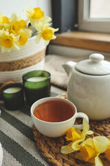 Cup of tea, candles, basket with daffodils, spring aesthetic photo