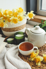 Obraz na płótnie Canvas Cup of tea, candles, open book, basket with daffodils, spring aesthetic photo