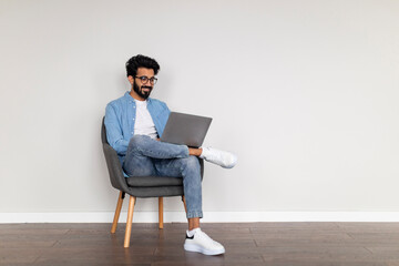 Freelance Career. Smiling Indian Man Using Laptop Computer While Sitting In Chair