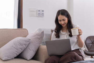 Attractive happy young Asian businesswomen at home, sitting at the desk, using a laptop computer, tablet and headphones having a video chat.